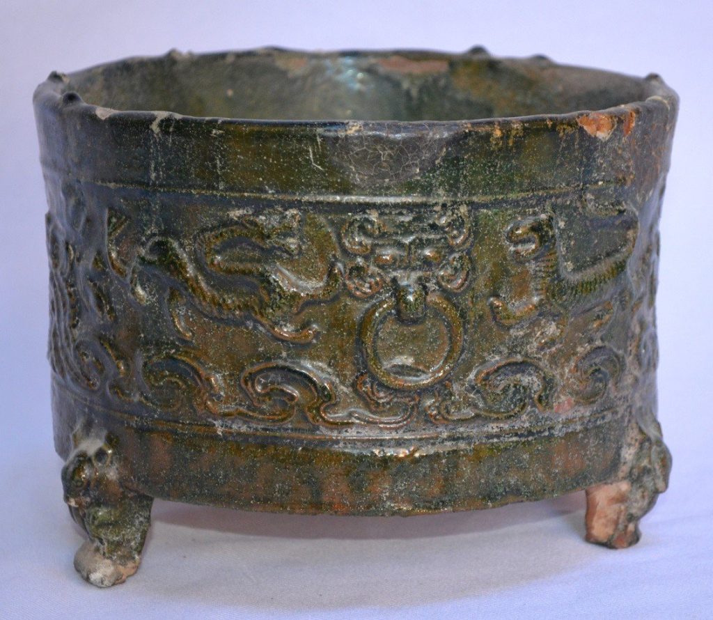 A green-glazed pottery tripod incense burner from the Han period. Decorated with a dragon and a tiger among other creatures. 