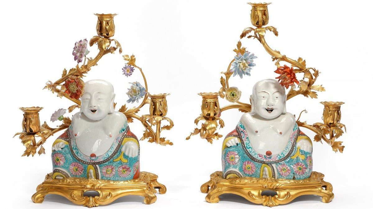 A pair of candelabras in gilt bronze from the mid-18th century. The arms are decorated with porcelain flowers from Vincennes. Porcelain buddhas from the Yongzheng period (1723-1735) sit in front of them.