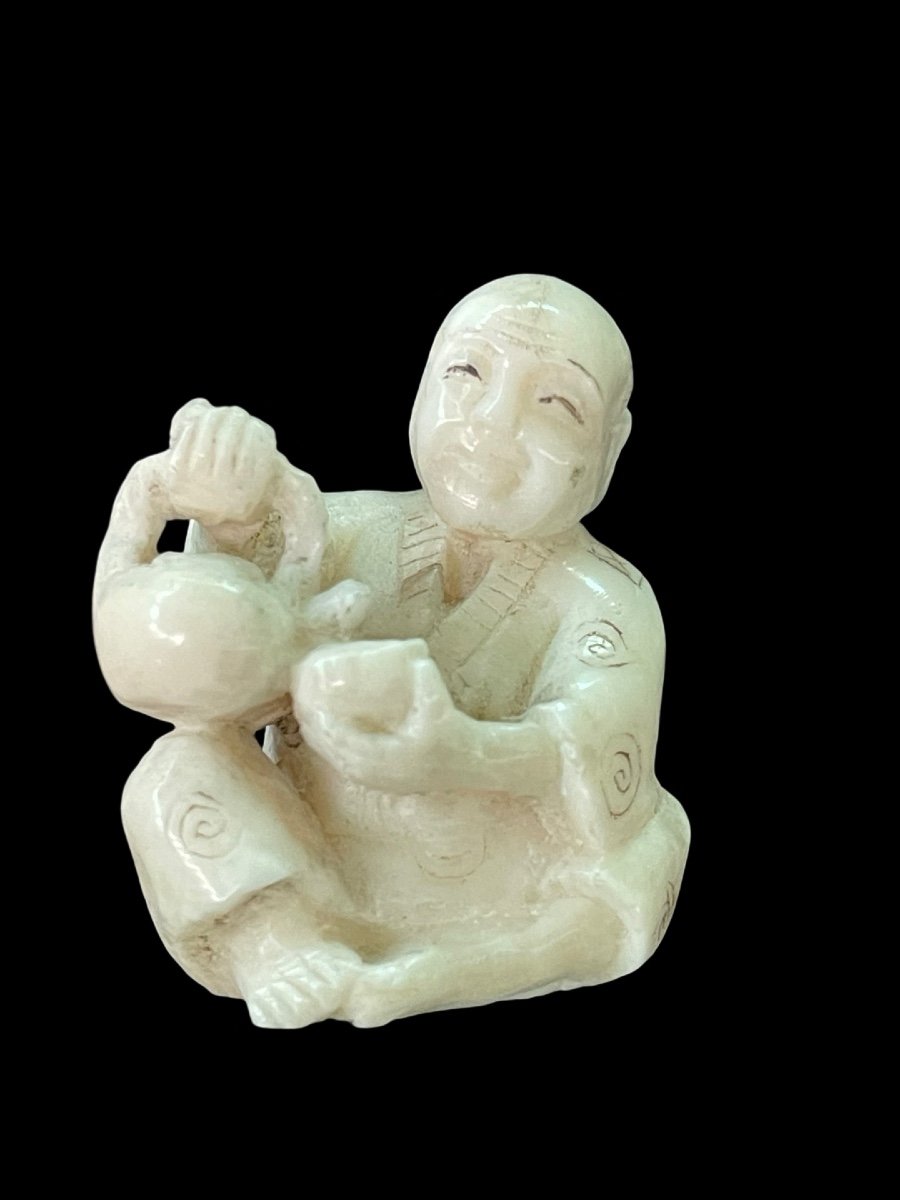 Ivory Netsuke Depicting A Seated Male Figure Pouring Tea. 